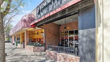 Fachada de Jimmy John’s de ladrillo, con amplios ventanales y mesas al aire libre.