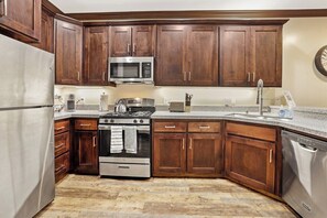 Una cocina con gabinetes de madera oscura, electrodomésticos de acero inoxidable y un suelo con estampado tipo espiga.