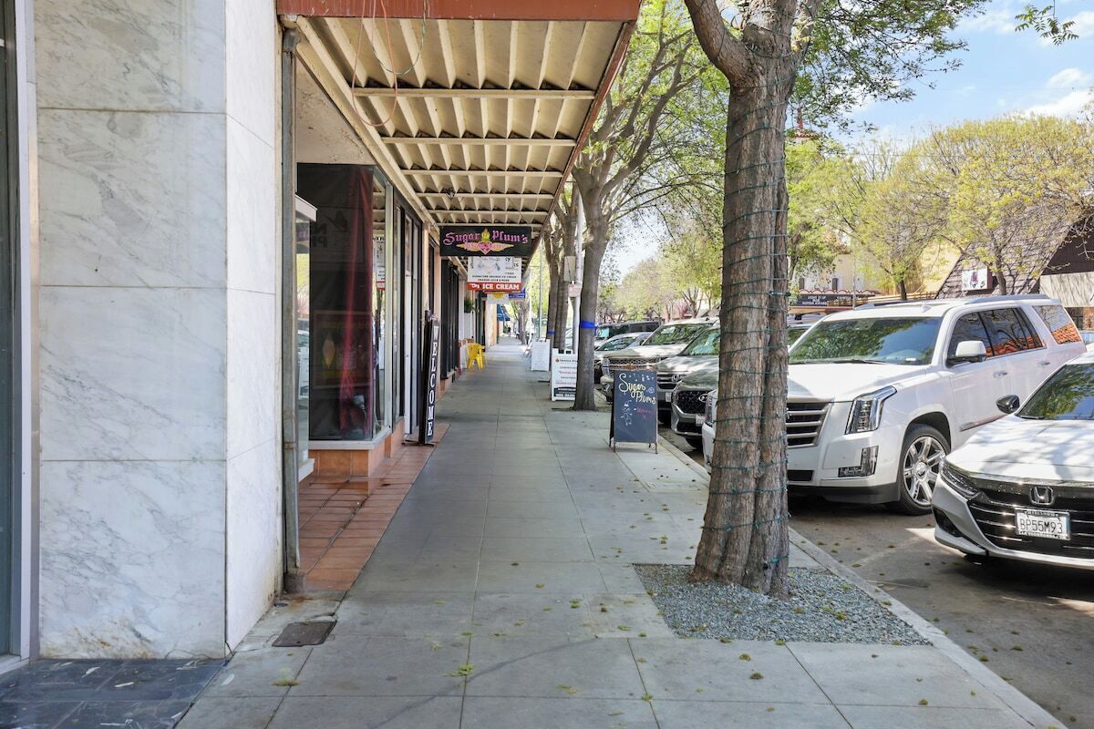 Un trottoir bordé de voitures garées et un bâtiment sur lequel on peut lire l’enseigne « Sugar Plum’s ».