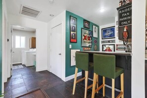 Una cocina con pared verde, una zona de bar con dos sillas verdes y diversos recuerdos enmarcados.