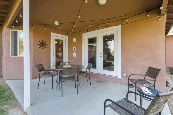 An outdoor patio with a round table and chairs, string lights, and decorative wall elements.