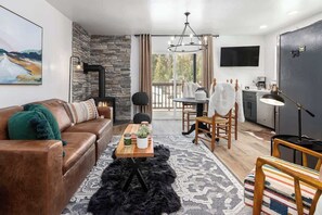 Un salon moderne avec un mur en pierre, une cheminée, un canapé, une table basse et une vue à travers une porte vitrée.