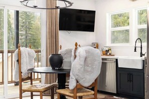 Une cuisine moderne équipée d’un téléviseur, d’une table à manger avec des chaises, d’une grande fenêtre et offrant une vue sur la verdure.