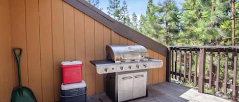 An outdoor grill area with a wooden deck, a shovelful of dirt, and a cooler.