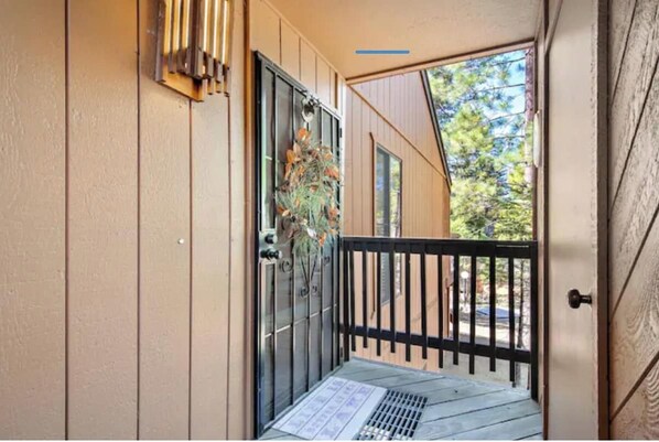 A wooden door with a metal gate, a small step leading to a balcony, and a window with a view of trees.