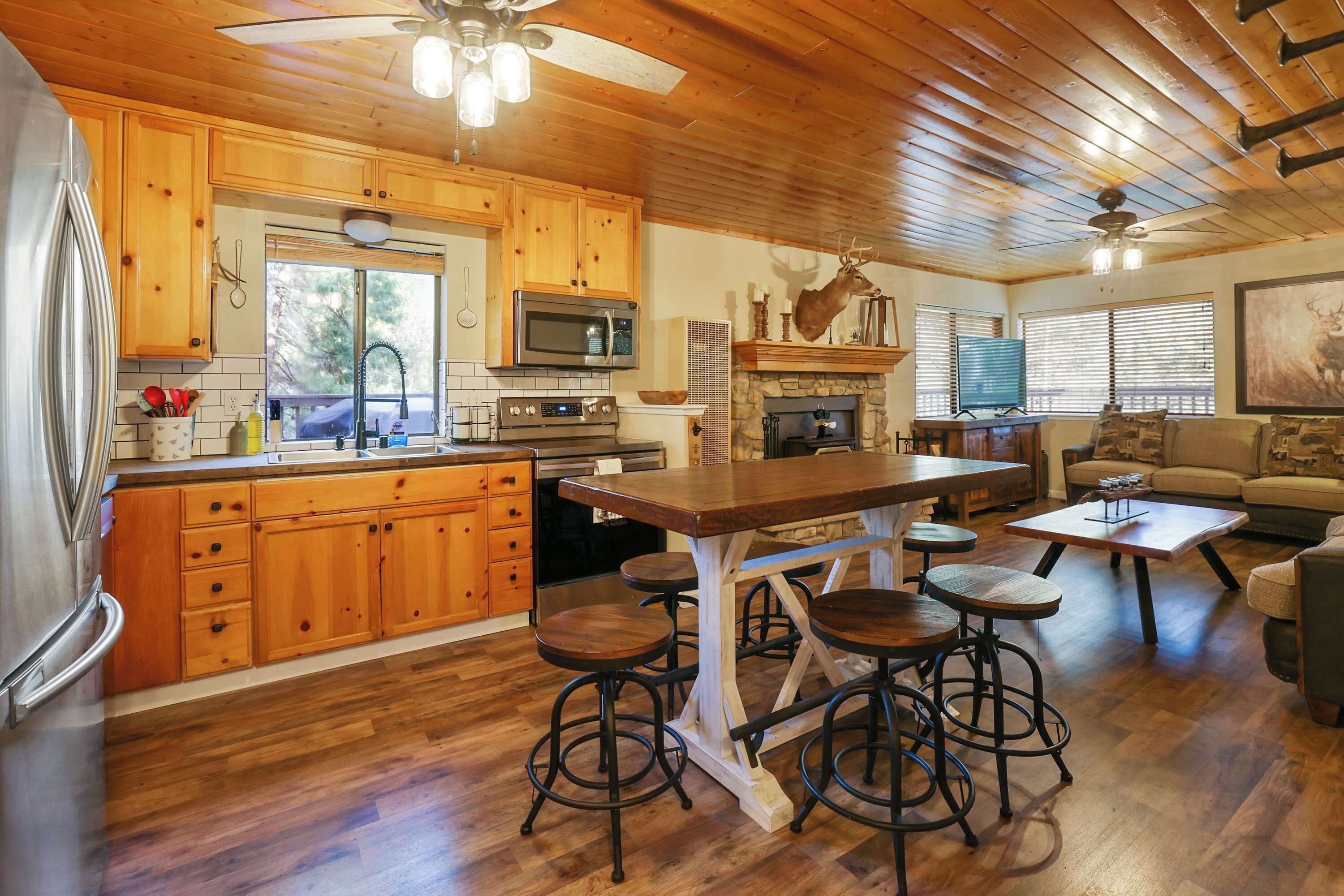 A spacious kitchen with wooden cabinets, a central island with stools, a microwave, and a stone fireplace.
