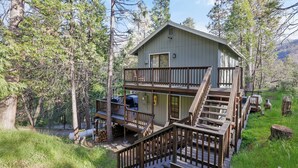 Eine zweistöckige Holzhütte mit einer Holzterrasse und Treppe, umgeben von Bäumen.