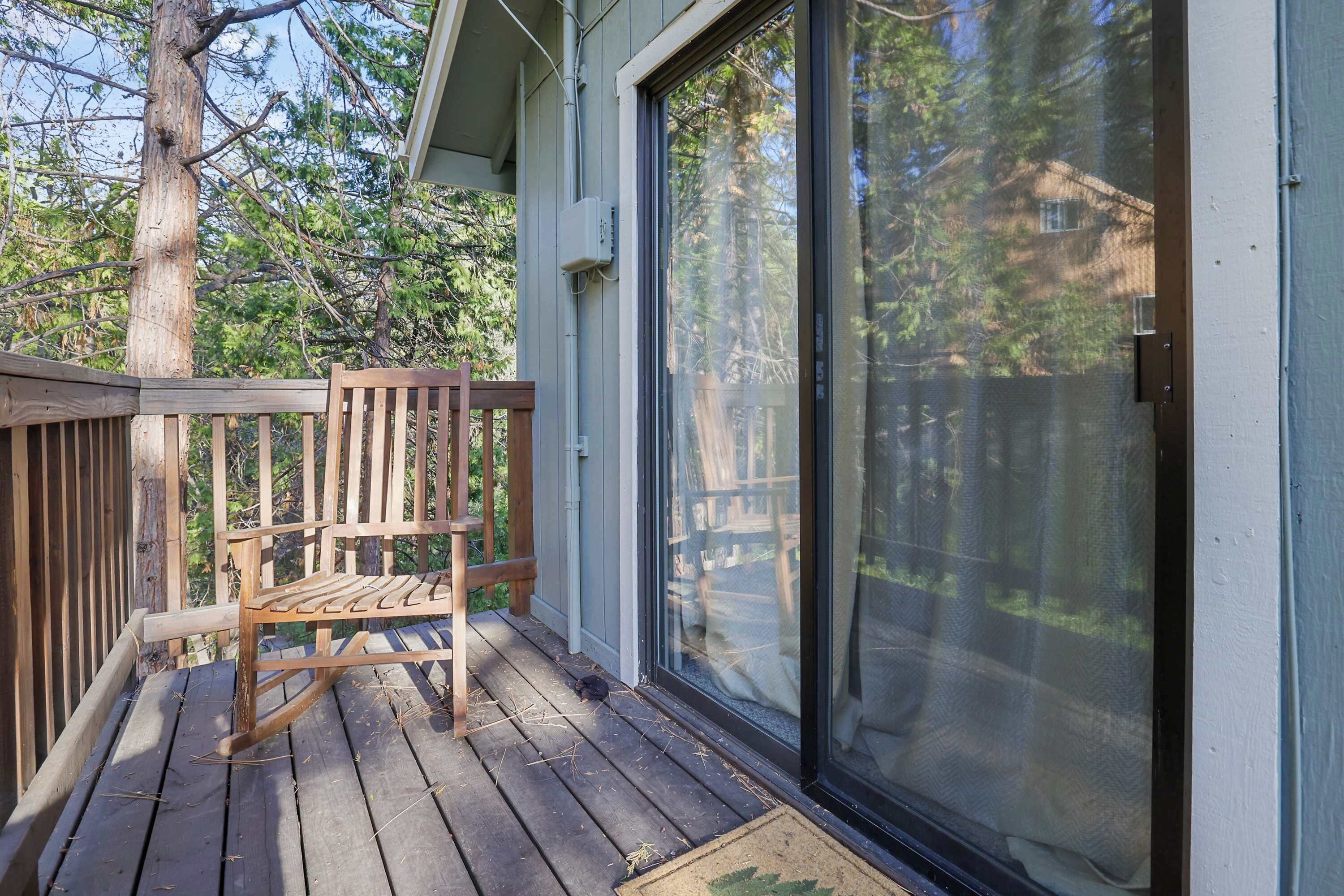 A wooden deck with a bench, a sliding glass door, and a tree in the background.