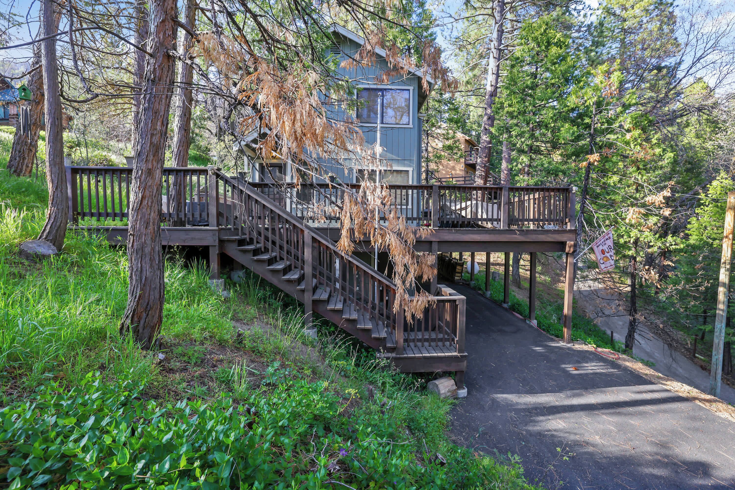 A cabin with a wooden staircase leading to a deck, surrounded by trees and greenery.