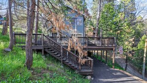 Eine Holzhütte mit einer Holztreppe, die zu einer Terrasse führt, umgeben von Bäumen und Grünflächen.