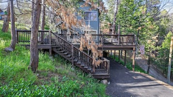 A cabin with a wooden staircase leading to a deck, surrounded by trees and greenery.