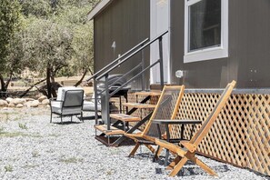 A building with a staircase leading to a door, outdoor seating with chairs and tables, and a wooden fence. - Tiny River House w River Frontage (Three River)