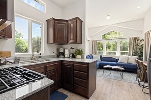 A modern kitchen with dark wood cabinets, a gas stove, and a large window. - Tiny River House w River Frontage (Three River)