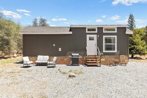 A single-story building with a patio area, outdoor seating, and a grill. - Tiny River House w River Frontage (Three River)