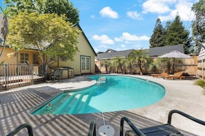 A swimming pool with a curved edge, surrounded by a patio area with lounge chairs and a wooden fence. - Downtown Retreat w/ Pool & Spa, Near National Parks (Visalia)