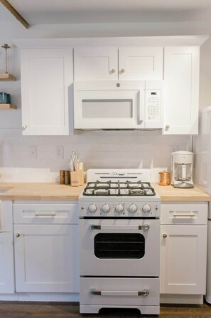 A kitchen with white cabinets, a gas stove, a microwave, and a coffee maker. - Downtown Retreat w/ Pool & Spa, Near National Parks (Visalia)
