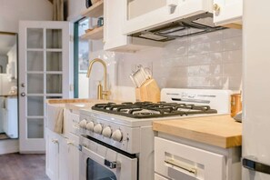 A kitchen with white cabinetry, a gas stove, an oven, and a coffee maker. - Downtown Retreat w/ Pool & Spa, Near National Parks (Visalia)