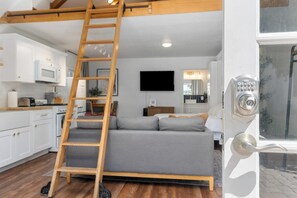A modern interior with a loft bed, a wooden ladder, a kitchen with white cabinets, and a door with a numeric keypad. - Downtown Retreat w/ Pool & Spa, Near National Parks (Visalia)