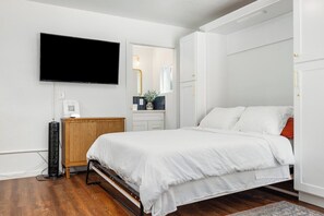 A bedroom with a bed, a TV mounted on the wall, a bedside table with a lamp, and a wardrobe.