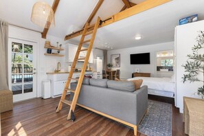A modern interior with a loft bed, a sofa, a dining area, and a kitchen.