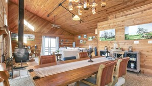 A wooden interior with a large dining table, chairs, a fireplace, and framed pictures on the walls.