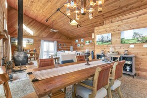 A wooden interior with a large dining table, chairs, a fireplace, and framed pictures on the walls.