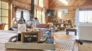 A wooden interior with a table set with wine glasses, a bottle, a box of marshmallows, and a welcome sign.