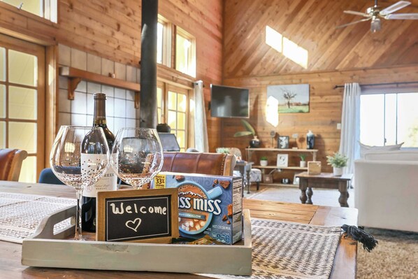 A wooden interior with a table set with wine glasses, a bottle, a box of marshmallows, and a welcome sign. - Sierra Nevada Cabin: Arcade & Jacuzzi (Shaver Lake)