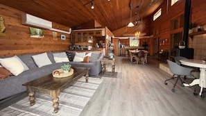 A cozy interior with a wooden ceiling, a sofa set, a dining area, and a kitchen. - Sierra Nevada Cabin: Arcade & Jacuzzi (Shaver Lake)