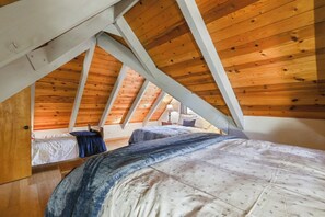 A bedroom with a sloped ceiling, wooden beams, and two beds.