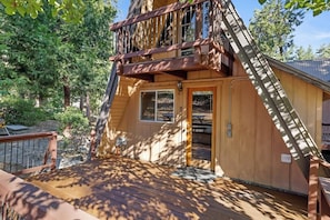 A wooden cabin with a deck, a staircase, and a door leading to an outdoor area.