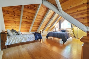 A bedroom with two beds, wooden flooring, and a sloped ceiling.
