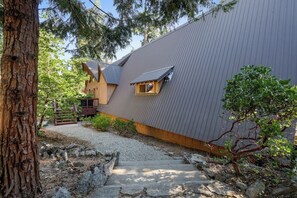 A modern building with a sloped roof, a small window, and a stone pathway leading to the entrance.