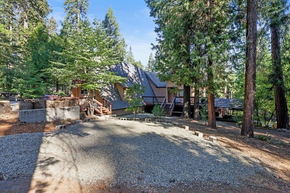 A cabin surrounded by trees with a gravel driveway leading to a wooden staircase.