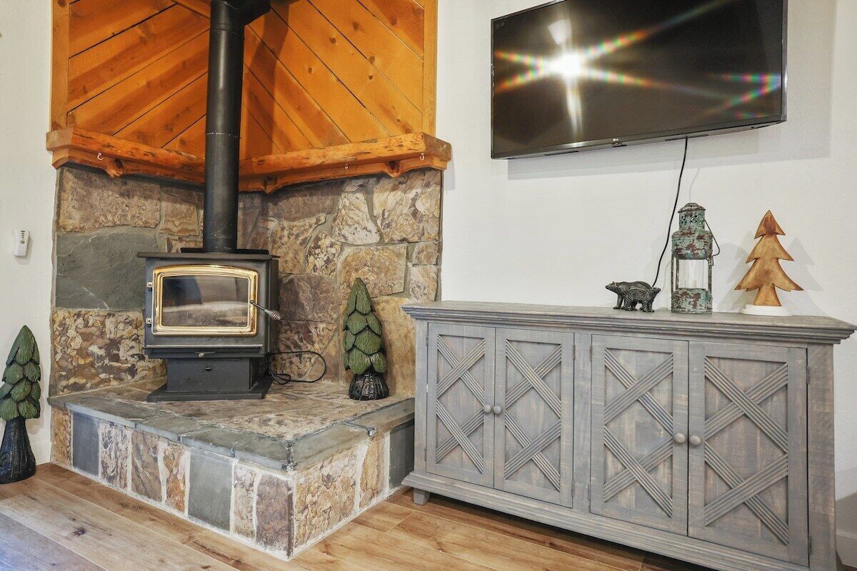 A stone fireplace with a black chimney, a television mounted on the wall, and a wooden cabinet with decorative items.