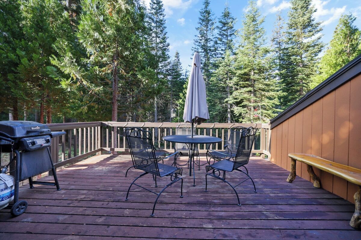 A wooden deck with a round table and chairs, a grill, and an umbrella.