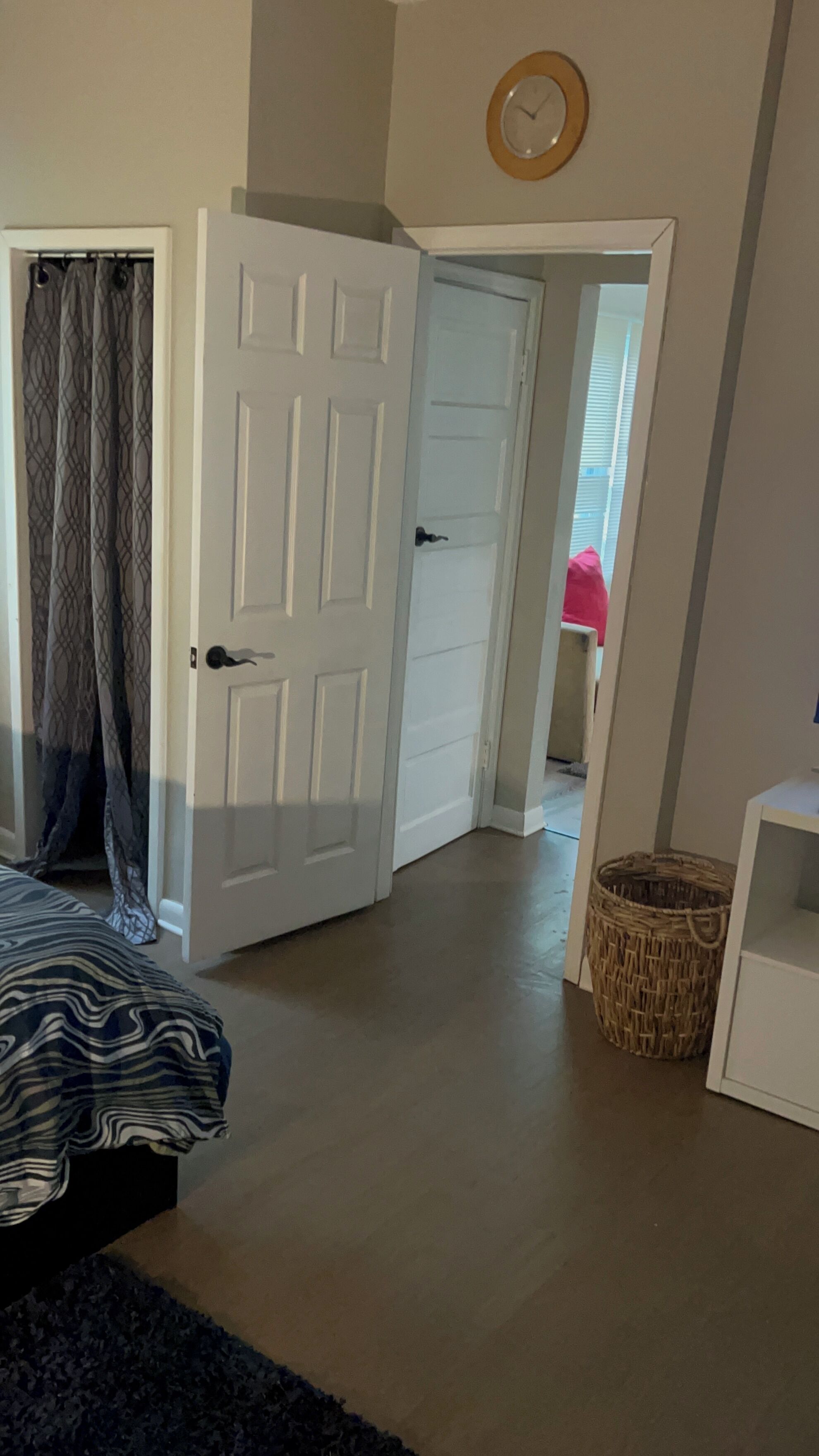 Een slaapkamer met een bed, een kledingkast, een deur en een rieten mand.