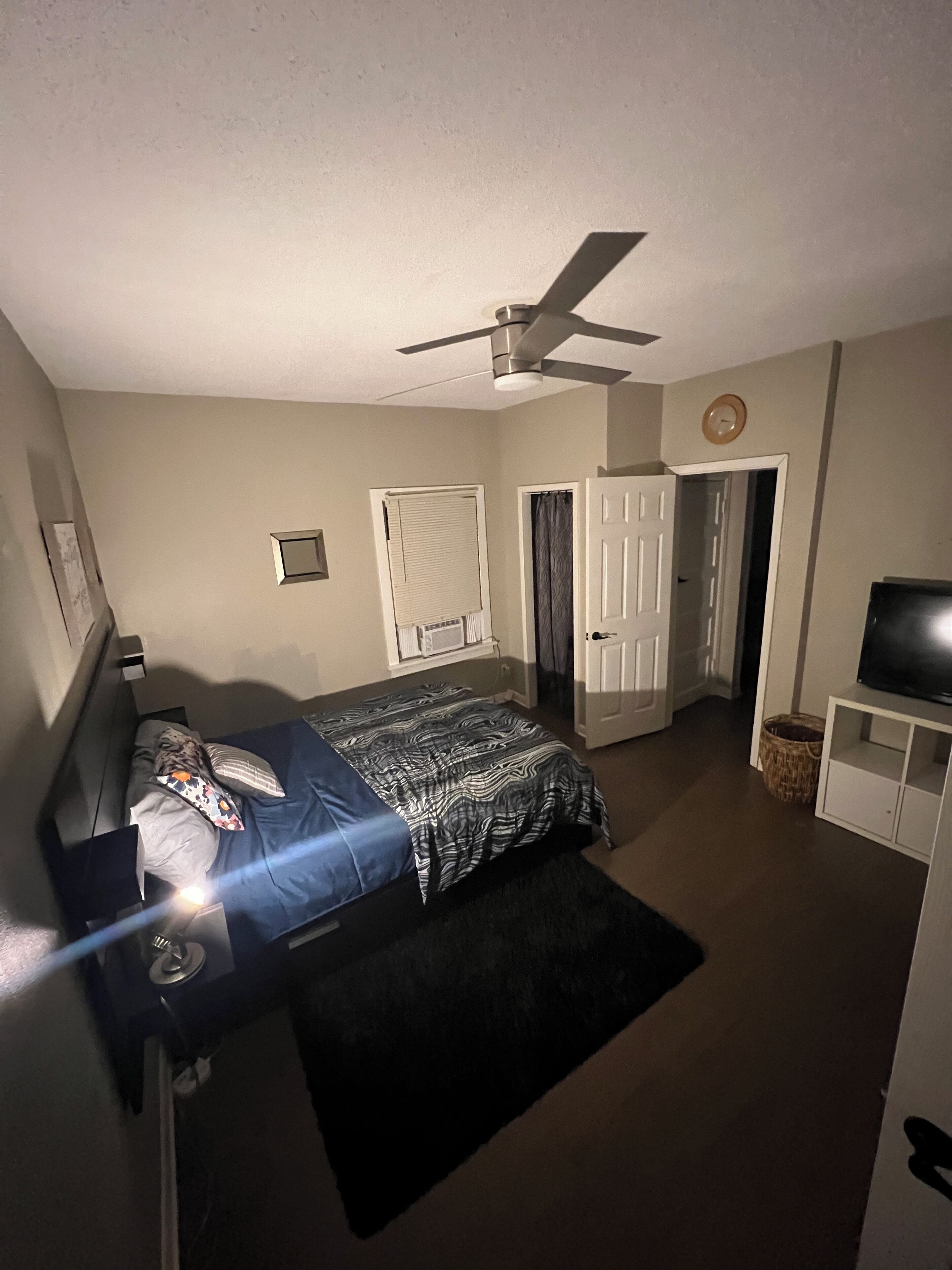 Ein Schlafzimmer mit Bett, Deckenventilator, Fernseher und einer Tür zu einem anderen Raum.