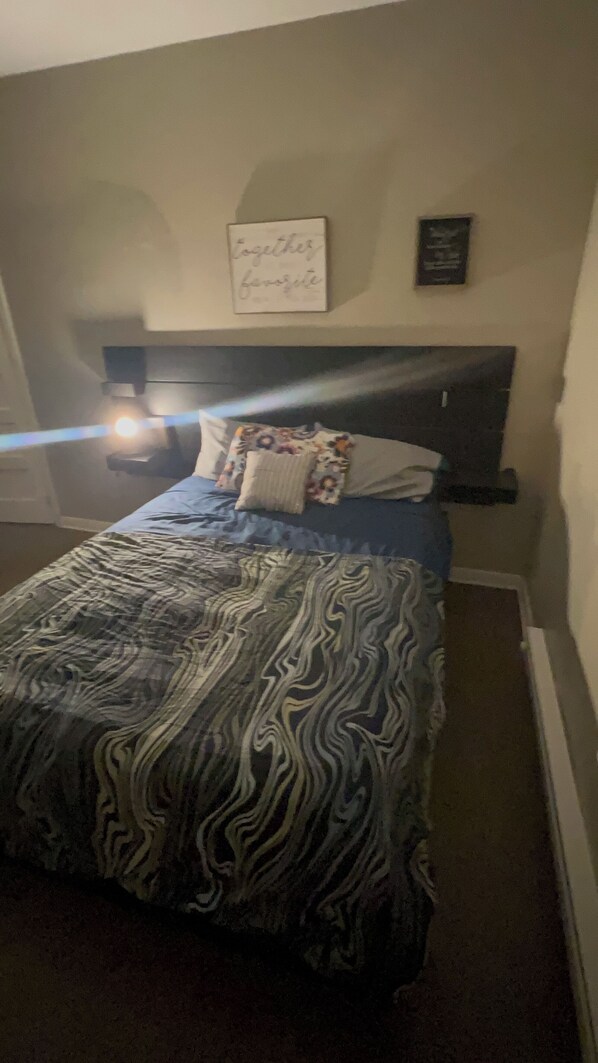 Une chambre à coucher avec un lit, une tête de lit, un panneau décoratif fixé au mur et une table de chevet.
