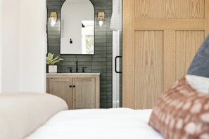 A bedroom with a bed, a wooden wardrobe, a mirror, a sink, and a potted plant.