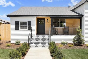 A single-story house with a front porch, a door with a wreath, and a small garden with shrubs.