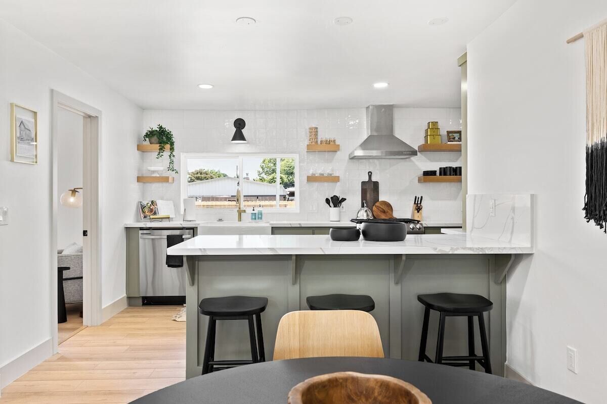A modern kitchen with a central island, black bar stools, and a dining table.