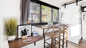 Een moderne keuken met een houten tafel, barkrukken, een raam met gordijnen en een lijst met een afbeelding aan de muur.