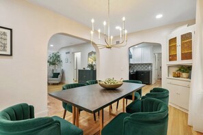 A dining area with a dark wooden table, green upholstered chairs, and a chandelier.