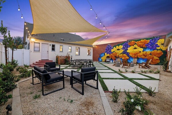 A patio area with outdoor furniture, a large mural, and a house in the background.