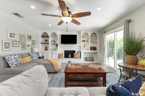 A living room with a fireplace, a ceiling fan, and a television.