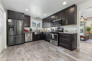 A modern kitchen with stainless steel appliances, dark cabinetry, and a marble countertop.