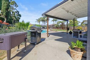 Une terrasse extérieure avec un barbecue, un espace salon abrité et une piscine en arrière-plan.
