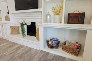 A living room with a fireplace, a television mounted above it, and shelves with decorative items and books.