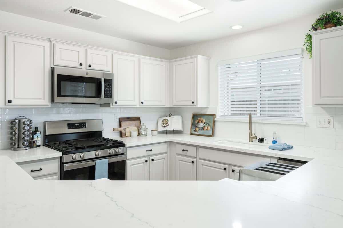 A modern kitchen with white cabinetry, stainless steel appliances, and a marble countertop.
